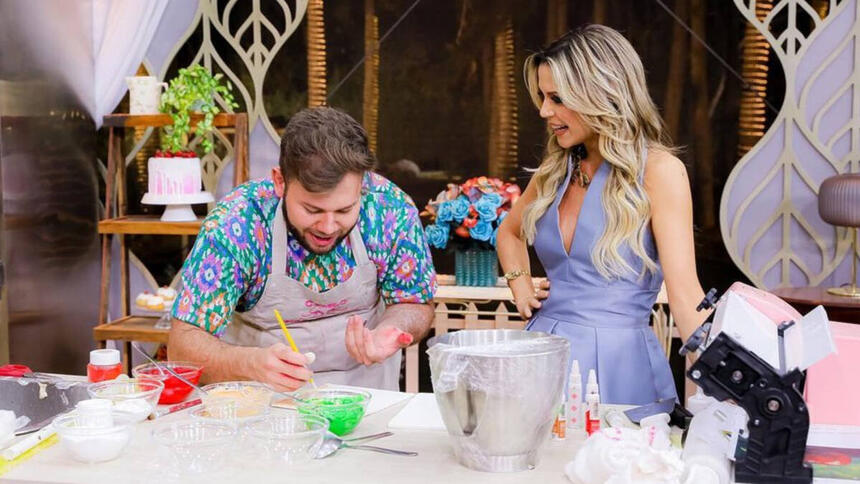 Camilo ao lado de Beca Milano, em frente a sua bancada, em trecho do episódio final do Bake Off Brasil