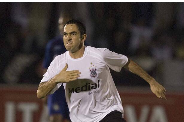 Chicão com camisa branca do Corinthians, batendo no peito com a mão direita durante jogo