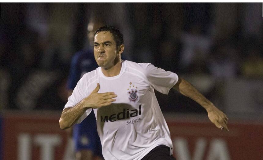 Chicão com camisa branca do Corinthians, batendo no peito com a mão direita durante jogo