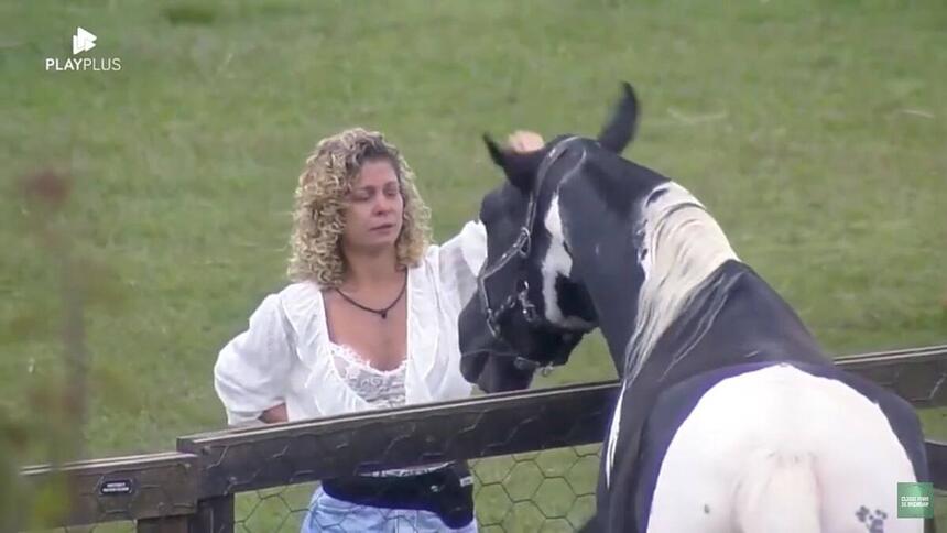 Bárbara Borges vestida com uma blusa branca e short jeans de frente para o cavalo Colorado.