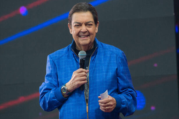 Fausão com um casaco azul, sorriso aberto, em trecho do programa Faustão na Band