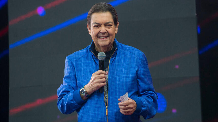 Fausão com um casaco azul, sorriso aberto, em trecho do programa Faustão na Band