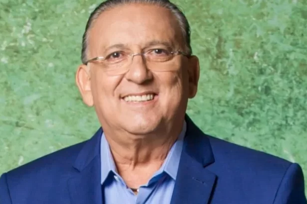 Galvão Bueno de blazer azul e camisa social branca, de óculos de grau, sorrindo durante sessão de fotos da TV Globo