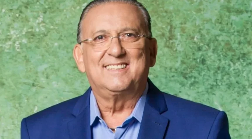 Galvão Bueno de blazer azul e camisa social branca, de óculos de grau, sorrindo durante sessão de fotos da TV Globo