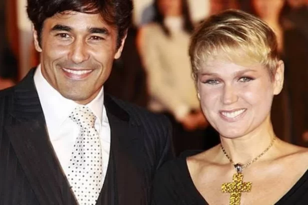 Luciano Szafir de paletó preto, camisa e gravata brancos, sorrindo durante cerimonia com Xuxa, de cabelo curto, sorrindo, usando vestido decotado preto e colar de brilhantes