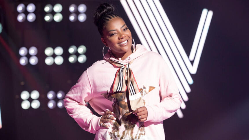 Ludmilla, com uma roupa rosa e um sorriso no rosto, no palco do The Voice+