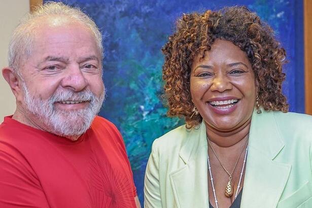 Lula com camisa básica vermelha, sorrindo, ao lado de Margareth Menezes, de blazer verde, sorrindo durante reunião em Brasília