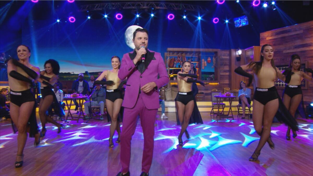 Maurício Manieri de terno e calça lilás, camisa social preta, segurando o microfone durante performance no Boteco do Ratinho, do SBT