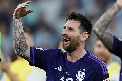 Messi, com um braço esquerdo erguido, sorrindo e comemorando a classificação da Argentina na Copa