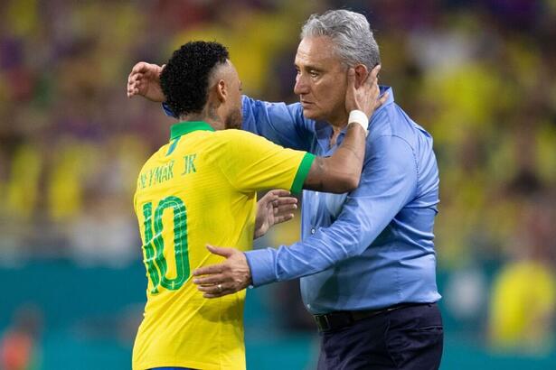 Neymar de costas, com a camisa da seleção brasileira, com a mão direita no pescoço de Tite e Tite de camisa social azul, calça branca, com a mão direita pra cima