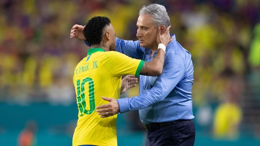 Neymar de costas, com a camisa da seleção brasileira, com a mão direita no pescoço de Tite e Tite de camisa social azul, calça branca, com a mão direita pra cima