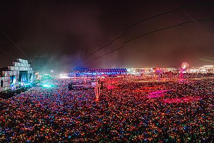 Palco Mundo do Rock in Rio visto de cima pela lente de um drone, cercado por uma multidão com pulseira de LED durante show de Coldplay