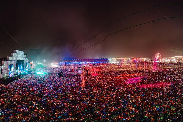 Palco Mundo do Rock in Rio visto de cima pela lente de um drone, cercado por uma multidão com pulseira de LED durante show de Coldplay