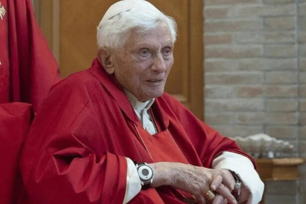 Papa Bento XVI, de batina, sentado em um evento da Igreja Católica