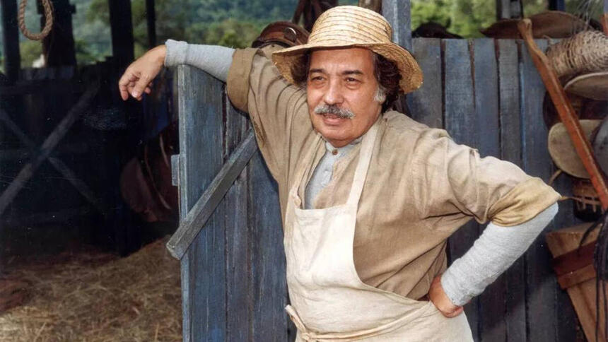 Ator Pedro Paulo Rangel, como o personagem Calixto, em frente uma cerca, na novela O Cravo e a Rosa