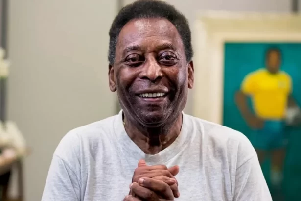 Pelé de camisa cinza, com as mãos juntas, sorrindo durante ensaio fotográfico
