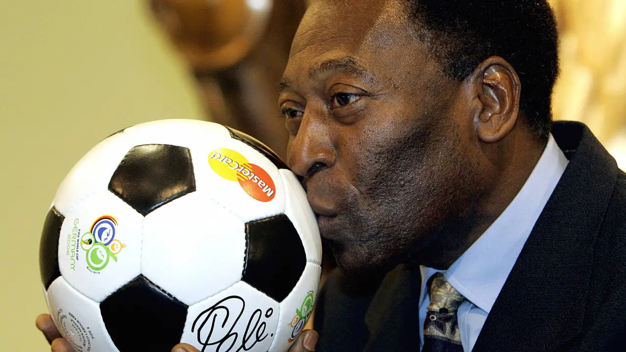 Pelé, de terno, beijando uma bola