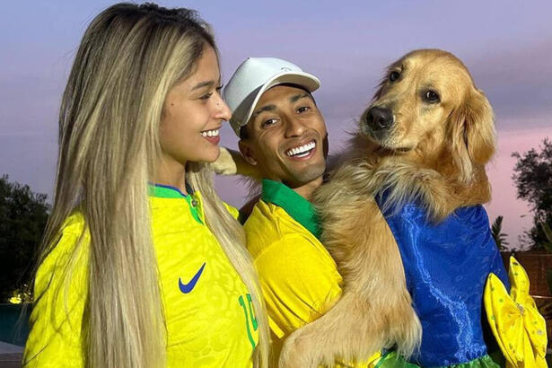 Raphinha, ao lado da esposa, e segurando a cachorra do casal no colo, em foto posada