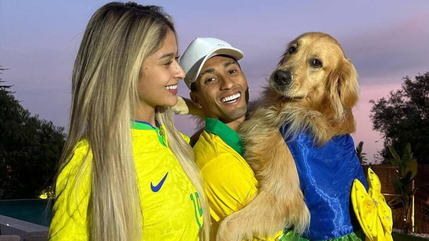 Raphinha, ao lado da esposa, e segurando a cachorra do casal no colo, em foto posada