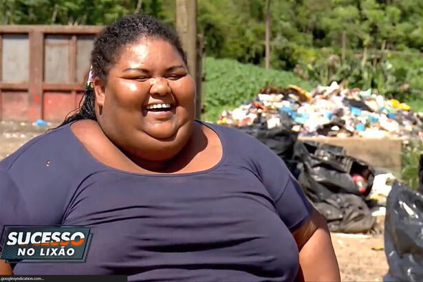 Roseli, com uma roupa azul e um sorriso no rosto, com um lixão ao fundo, em trecho da entrevista para o Domingo Espetacular