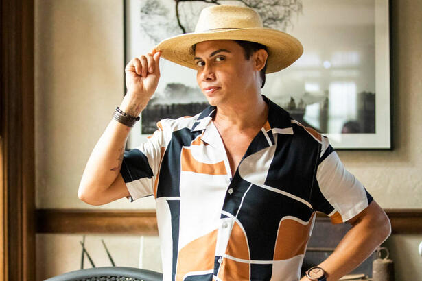 Silvero Pereira, com uma roupa estampada e um chapéu na cabeça, posando como Zaquieu em trecho da novela Pantanal