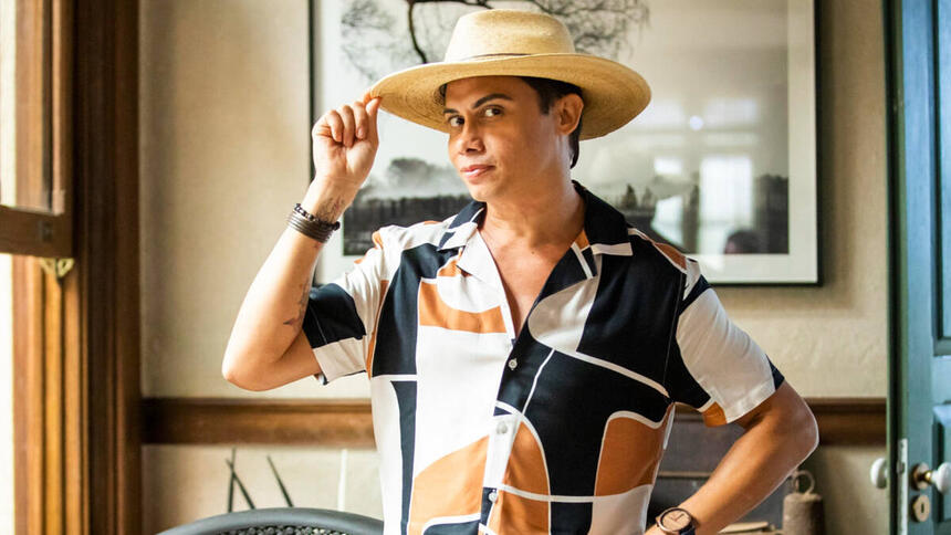 Silvero Pereira, com uma roupa estampada e um chapéu na cabeça, posando como Zaquieu em trecho da novela Pantanal