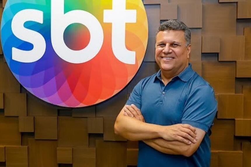 téo josé de camisa pólo azul, braços cruzados, sorrindo, ao lado da logo do SBT