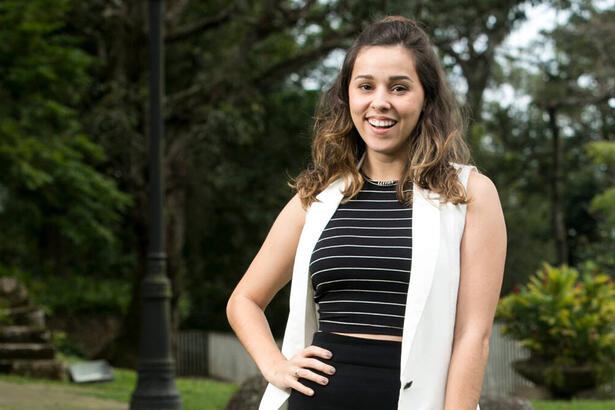 Thati Lopes, em uma foto posada, sorrindo, com a mão na cintura, com um gramado ao fundo