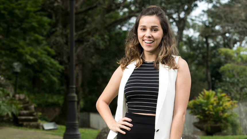 Thati Lopes, em uma foto posada, sorrindo, com a mão na cintura, com um gramado ao fundo