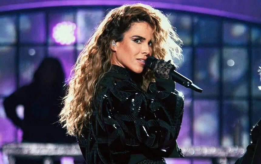 Wanessa com look preto brilhoso, cabelo ondulado, segurando um microfone durante performance no Música Boa Ao Vivo, do Multishow