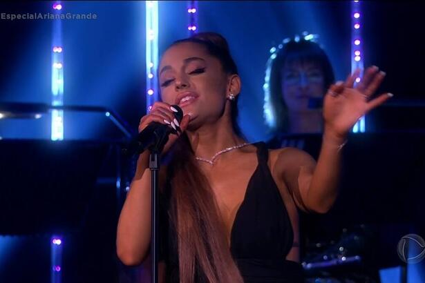 Ariana Grande levanta o braço esquerdo para canta no especial Live in London, exibido na Record TV