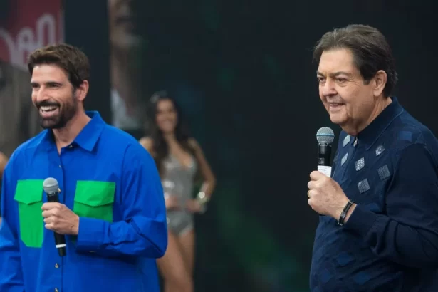 Ator Reynaldo Gianecchini de camisa azul ao lado do apresentador Faustão que sorrir para a câmera