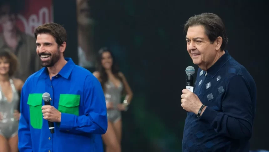 Ator Reynaldo Gianecchini de camisa azul ao lado do apresentador Faustão que sorrir para a câmera