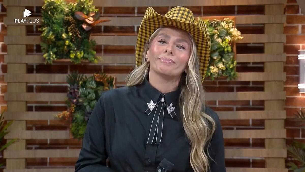 Galisteu de blusa preta e chapéu de fazendeira esperando para conversar ao vivo com os peões | Imagem: Reprodução/Record TV
