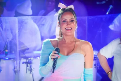 Claudia Leitte com look azul e rosa e laço rosa na cabeça durante performance em trio elétrico no Carnatal