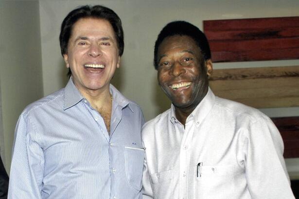 Pelé de branco junto com o Silvio Santos de camisa social azul e calça preta, ambos sorrindo para a foto