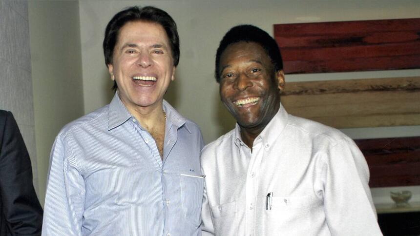 Pelé de branco junto com o Silvio Santos de camisa social azul e calça preta, ambos sorrindo para a foto