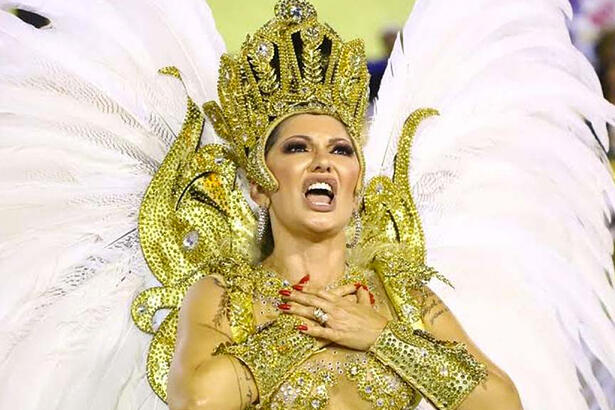 Antonia Fontenelle com as mãos no peito, usando look dourado de carnaval com asas coberta de plumas brancas