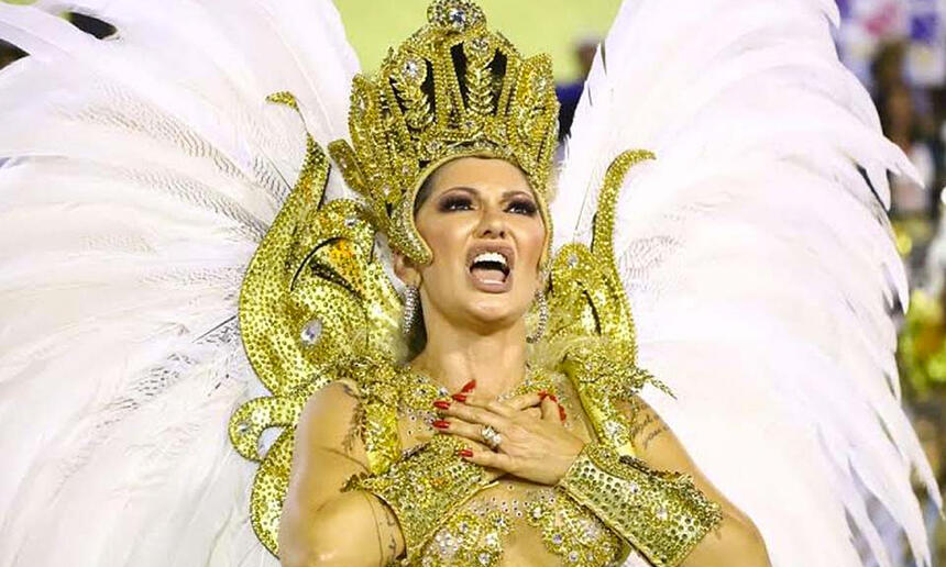 Antonia Fontenelle com as mãos no peito, usando look dourado de carnaval com asas coberta de plumas brancas