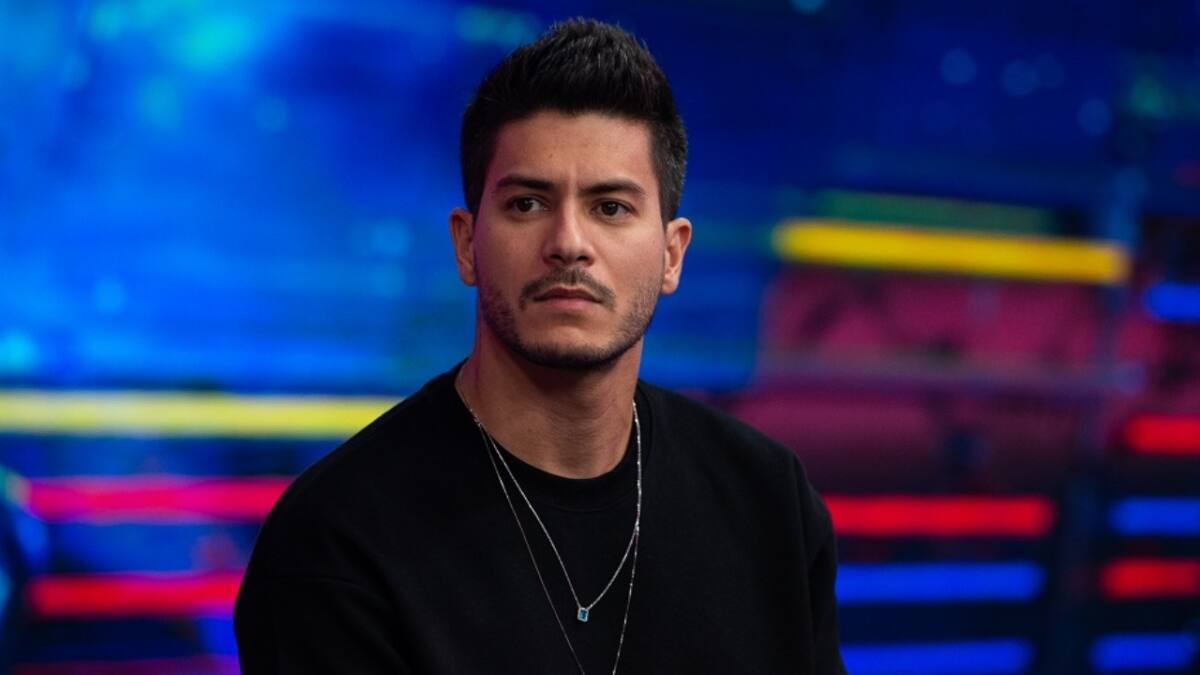 Arthur Aguiar de camisa manga longa preta, com um colar de prata, sentado, durante gravação de programa na TV Globo