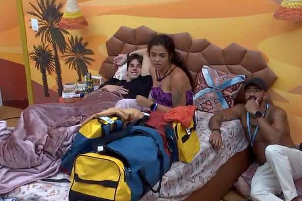 Gabriel Fop de camisa preta, deitado ao lado de Paula Freitas, de top roxo, ao lado de Ricardo de camisa preta e calça branca sentado no chão do Quarto Deserto do BBB 23