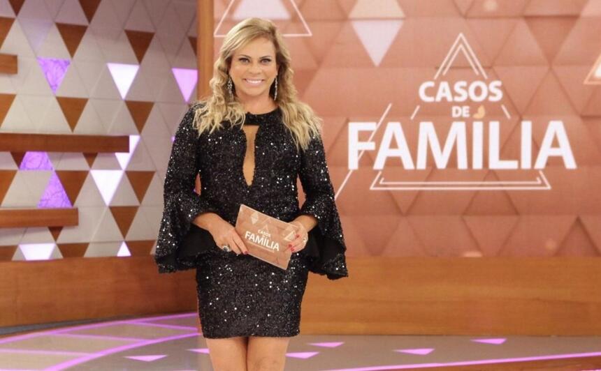 Christina Rocha de vestido preto, sorrindo, segurando plaquinhas durante gravação do Casos de Familia, do SBT