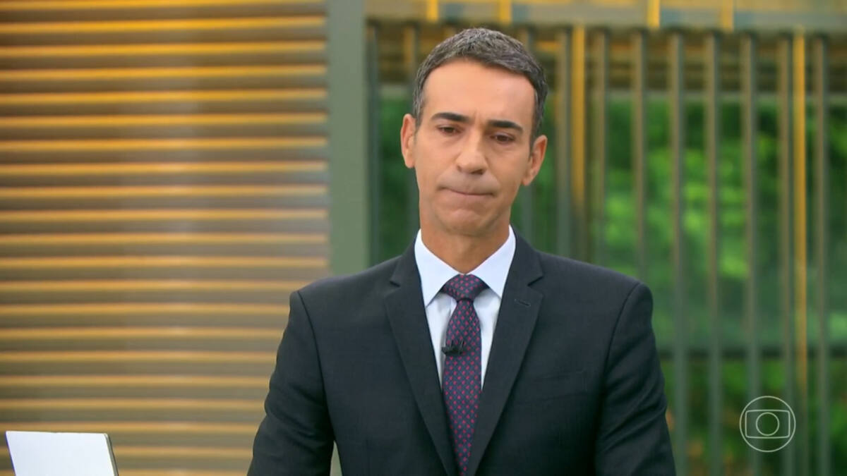 Cesar Tralli, de terno e gravata, com a cabeça olhando para baixo e feição triste, no estúdio do Jornal Hoje