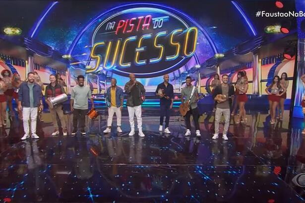 Palco do Faustão Na Band com a Turma do Pagode no início de sua apresentação musical. No canto do palco está Fausto Silva com roupa escura.