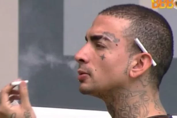 MC Guimê fumando, sentado, dentro da casa do BBB 23, com cigarro na orelha, soltando fumaça pelo nariz