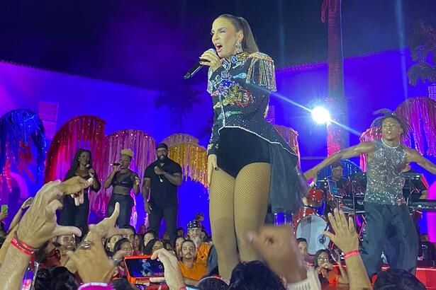 Ivete Sangalo de look preto com brilhantes, cabelo preso, segurando o microfone durante gravação de EP