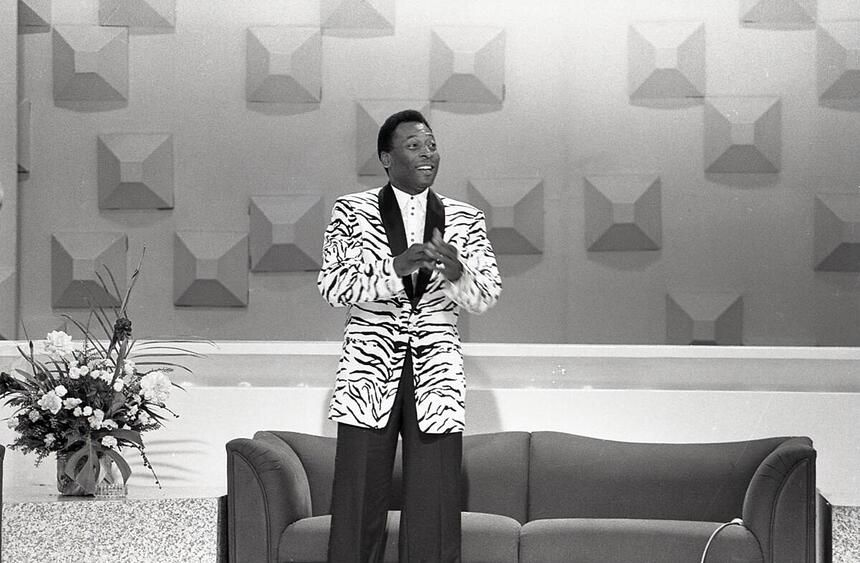 Pelé de pé, vestido com blazer branco e preto e calça preto, em participação no programa da Hebe, no SBT.