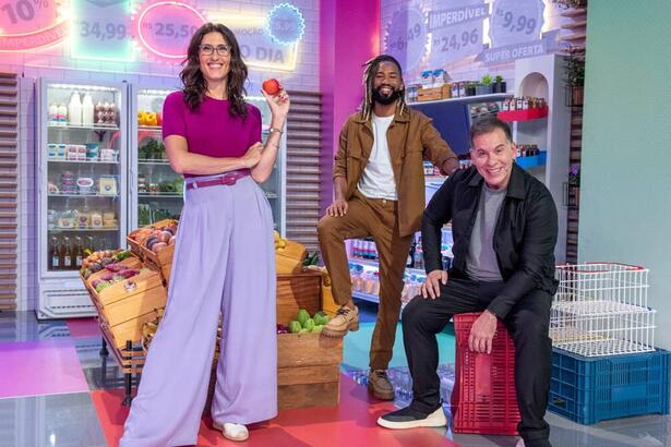 Paola vestida de camisa roxa e calça com o chef João de camisa branca com casaco e calça marrom e o ator Leandro Hassum de roupa preta.