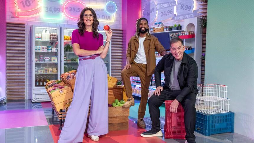 Paola vestida de camisa roxa e calça com o chef João de camisa branca com casaco e calça marrom e o ator Leandro Hassum de roupa preta.