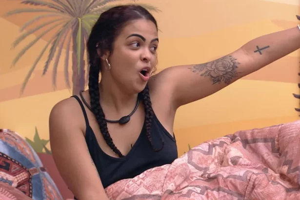 Paula Freitas de top preto, de trança, sentada na cama do Quarto Deserto, do BBB 23